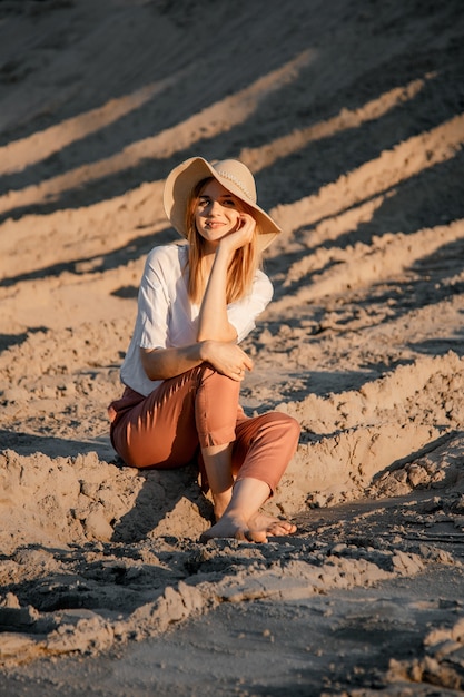 Jovem linda mulher solitária com cabelo comprido e chapéu de palha. uma garota solitária desce as dunas de areia.