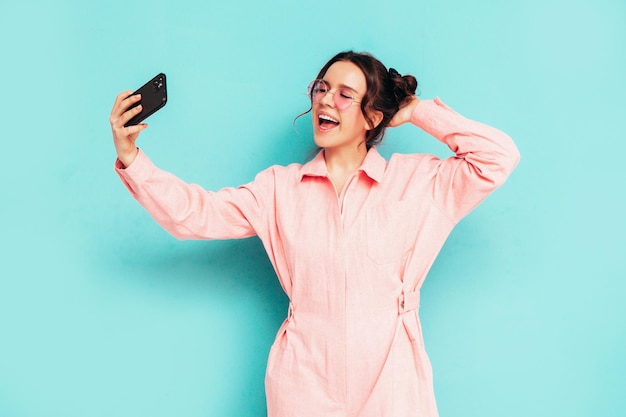 Jovem linda mulher sorridente em macacão rosa de verão na moda Mulher despreocupada sexy posando perto de parede azul em estúdio com dois chifres Modelo positivo se divertindo e enlouquecendo Alegre e feliz