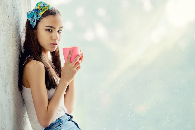 Jovem linda sentada na janela tomando café