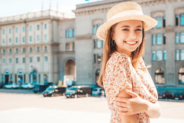 Jovem linda sorridente hipster em vestido de verão na moda Mulher despreocupada sexy posando no fundo da rua com chapéu ao pôr do sol Modelo positivo rindo ao ar livre Alegre e feliz