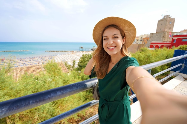 Jovem linda sorrindo feliz tira selfie pela câmera do smartphone na vila de Termoli, Itália