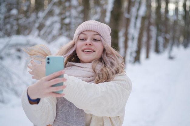 Jovem linda tira uma selfie em uma câmera de smartphone em um parque nevado