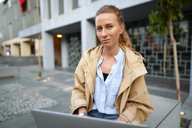 Jovem linda trabalhando em um laptop sentado no banco na rua