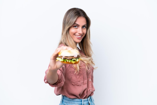 Jovem linda uruguaia segurando um hambúrguer isolado no fundo branco com expressão feliz