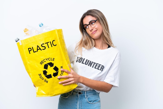 Jovem linda uruguaia segurando um saco cheio de garrafas plásticas para reciclar isoladas no fundo branco com expressão triste