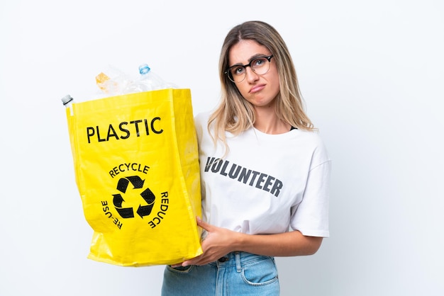 Jovem linda uruguaia segurando um saco cheio de garrafas plásticas para reciclar isoladas no fundo branco com expressão triste