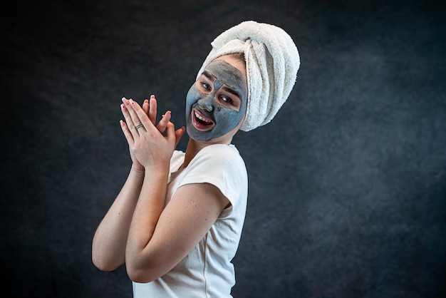 jovem linda usa toalha branca fazendo tratamento de beleza e bem-estar com máscara facial de barro preto