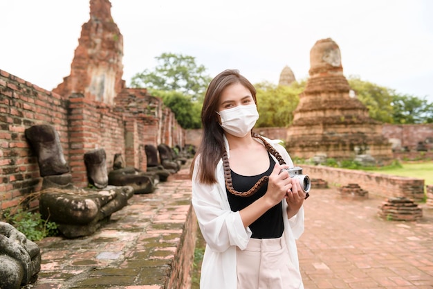 Jovem linda usando máscara protetora viajando e tirando fotos no histórico tailandês