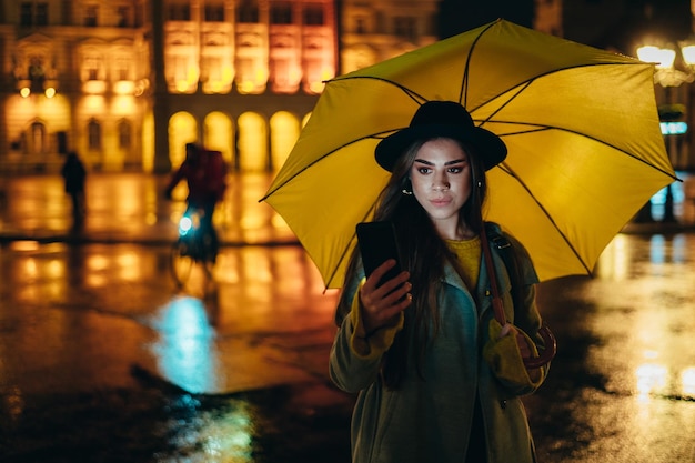 Foto jovem linda usando um smartphone e segurando um guarda-chuva amarelo