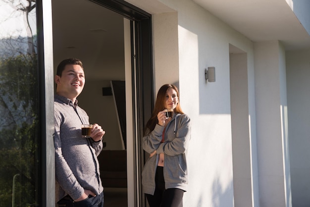 jovem lindo casal bonito desfrutando de café da manhã na porta de sua casa de luxo