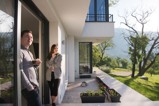 jovem lindo casal bonito desfrutando de café da manhã na porta de sua casa de luxo