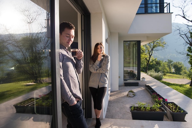 jovem lindo casal bonito desfrutando de café da manhã na porta de sua casa de luxo