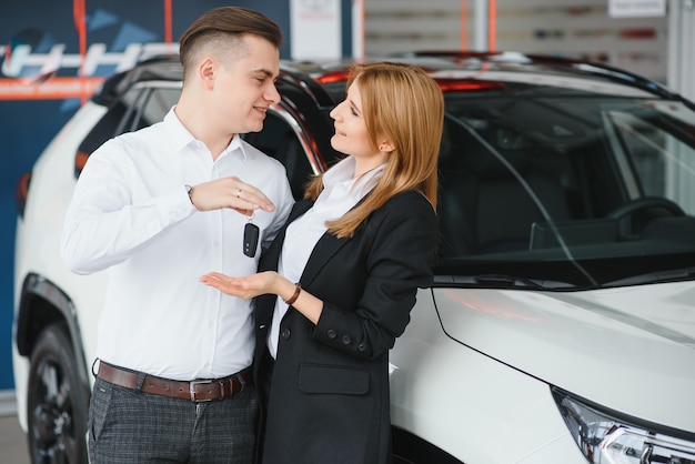 Jovem lindo casal feliz comprando um carro. marido comprando carro para sua esposa em um salão. conceito de compra de carro.