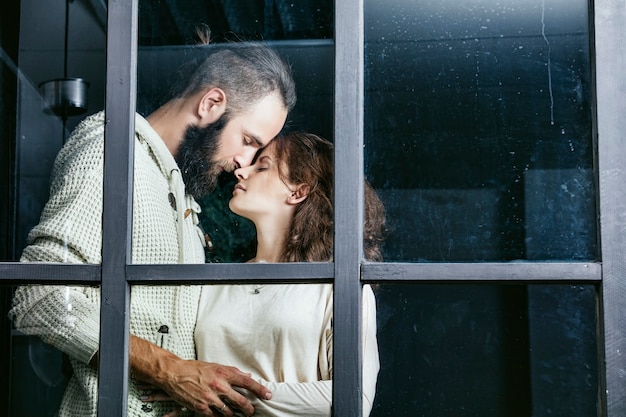 Jovem lindo casal heterossexual, homem e mulher, amantes se abraçando do lado de fora da janela