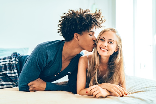 Jovem lindo casal inter-racial relaxado deitado na cama abraçado