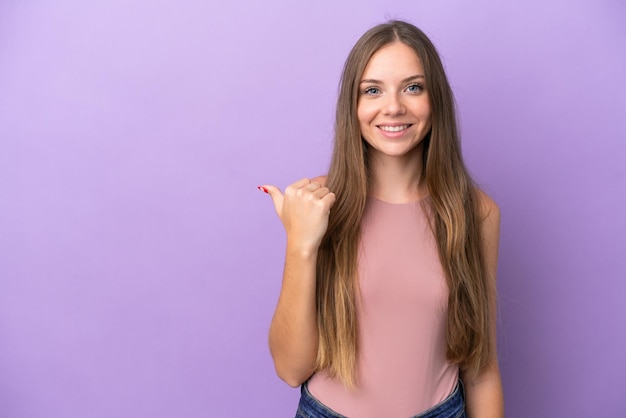 Jovem lituana isolada em fundo roxo apontando para o lado para apresentar um produto