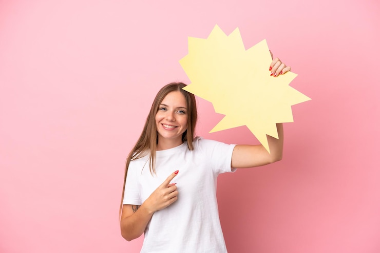 Foto jovem lituana isolada em um fundo rosa segurando um balão de fala vazio e apontando-o