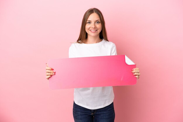 Jovem lituana isolada em um fundo rosa segurando um cartaz vazio