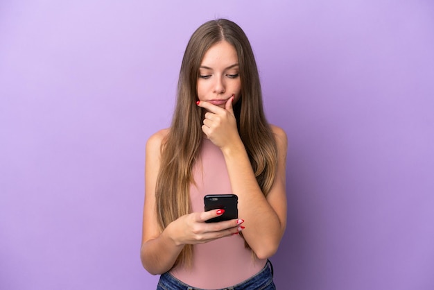 Jovem lituana isolada em um fundo roxo pensando e enviando uma mensagem