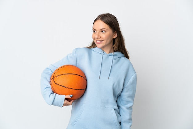 Jovem lituana jogando basquete isolada na parede branca, olhando para o lado e sorrindo