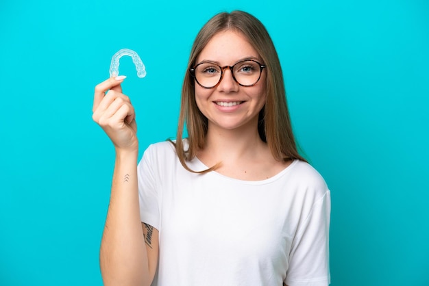 Jovem lituana segurando aparelhos invisíveis isolados em fundo azul sorrindo muito