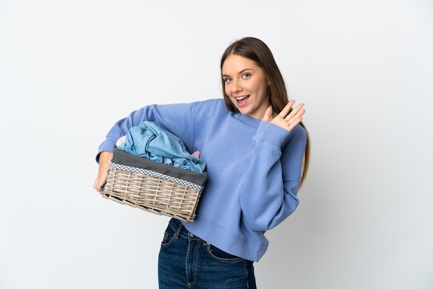 Foto jovem lituana segurando um cesto de roupas, isolado no fundo branco, saudando com a mão com expressão feliz