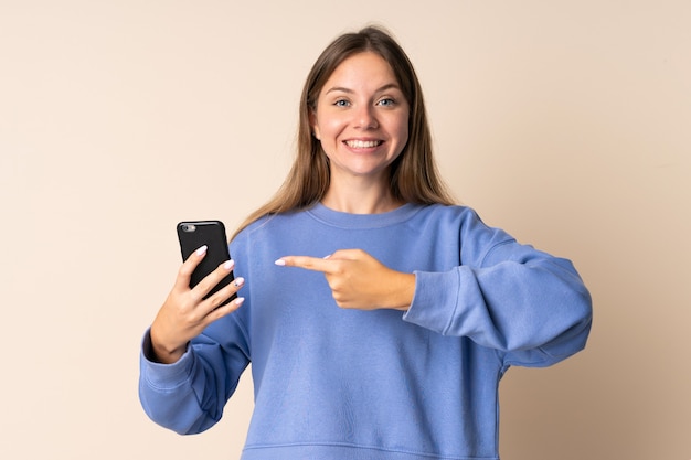 Jovem lituana usando um celular bege e apontando para ele