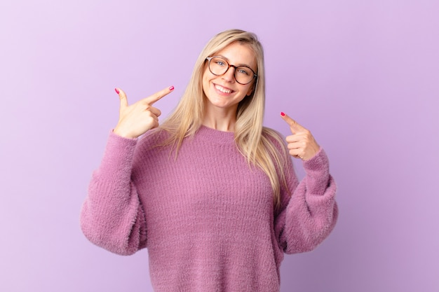 Jovem loira a sorrir com confiança a apontar para o seu largo sorriso