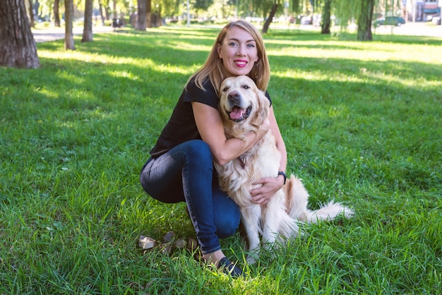 Jovem loira abraça seu cachorro. Retriever de raça de cachorro com uma garota no parque.