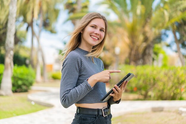 Jovem loira ao ar livre tocando a tela do tablet com expressão feliz