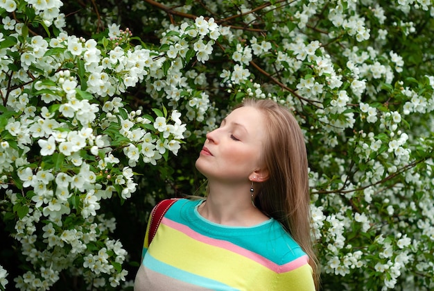 Jovem loira apreciando o perfume de flores de macieira