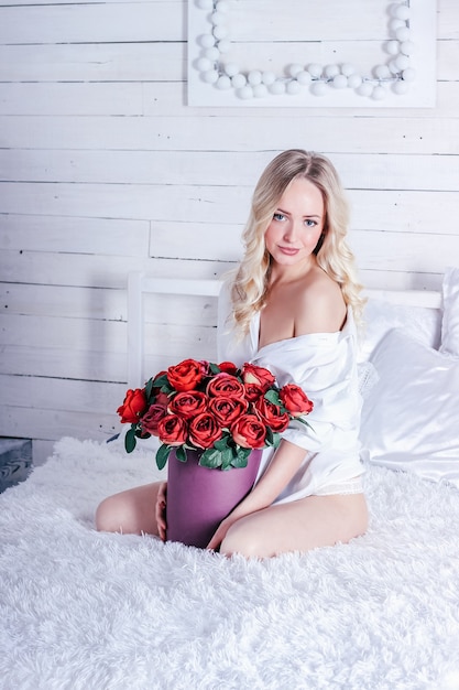 Jovem loira atraente com muitas rosas na cama