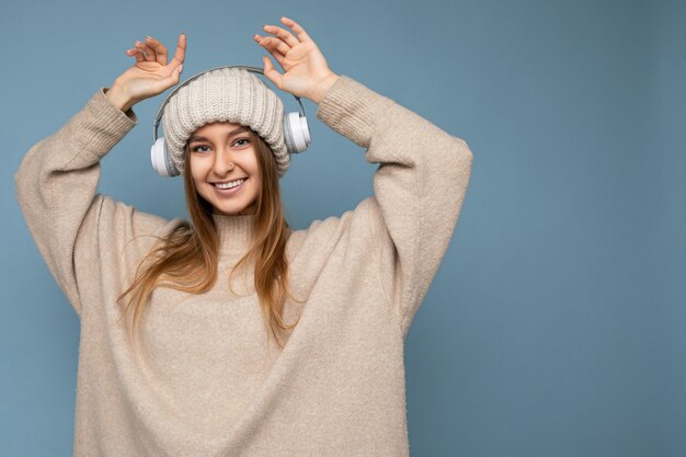 Jovem loira atraente e sorridente, vestindo um suéter bege de inverno e um chapéu