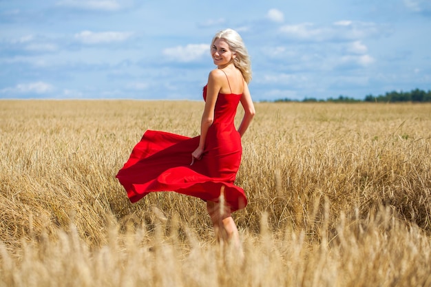 jovem loira bonita em um vestido vermelho posando em um campo de trigo