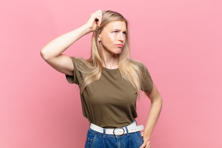 Foto jovem loira bonita se sentindo perplexa e confusa, coçando a cabeça e olhando para o lado