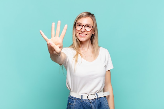 Jovem loira bonita sorrindo e parecendo amigável, mostrando o número quatro ou o quarto com a mão para a frente, em contagem regressiva