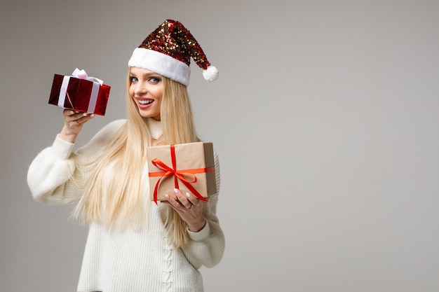 jovem loira caucasiana com chapéu de Papai Noel espumante segurando dois presentes