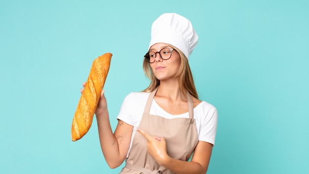 Jovem loira chef segurando uma baguete de pão