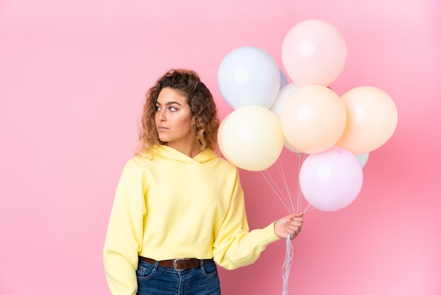Jovem loira com cabelo encaracolado pegando muitos balões isolados no lado rosa
