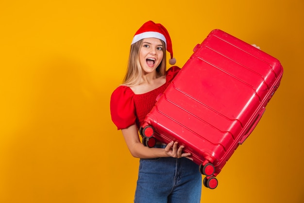 Jovem loira com roupa de natal e mala de viagem. conceito de viagem de natal