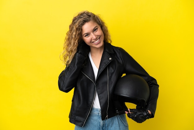 Jovem loira com um capacete de motociclista isolada em um fundo amarelo rindo