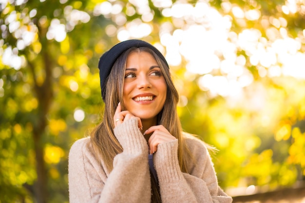 Jovem loira com um gorro de lã no outono ao pôr do sol em um espaço de cópia do parque natural