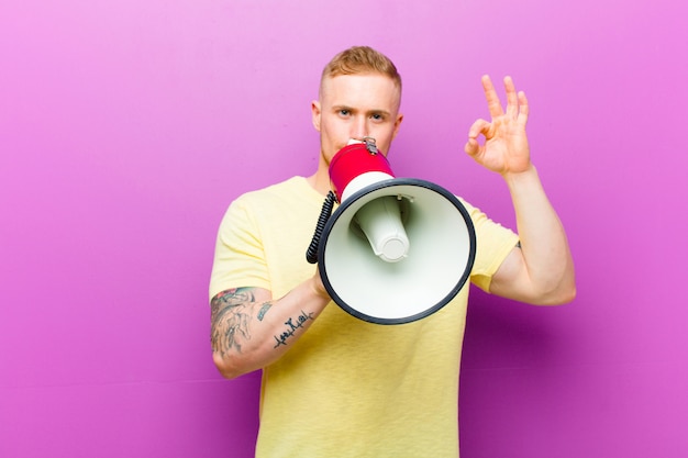 Jovem loira com um megafone, vestindo camiseta amarela contra fundo roxo