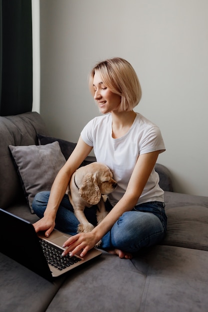 jovem loira com um spaniel sentada em um laptop blogueiro trabalhando no escritório doméstico na Internet