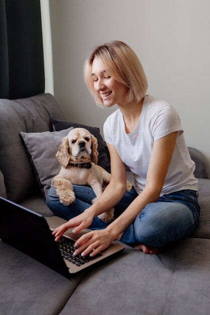 Jovem loira com um spaniel sentada em um laptop blogueiro trabalhando no escritório doméstico na internet