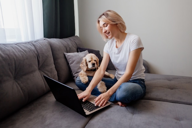 jovem loira com um spaniel sentada em um laptop blogueiro trabalhando no escritório doméstico na Internet