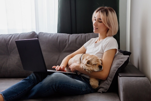 Jovem loira com um spaniel sentada em um laptop blogueiro trabalhando no escritório doméstico na internet