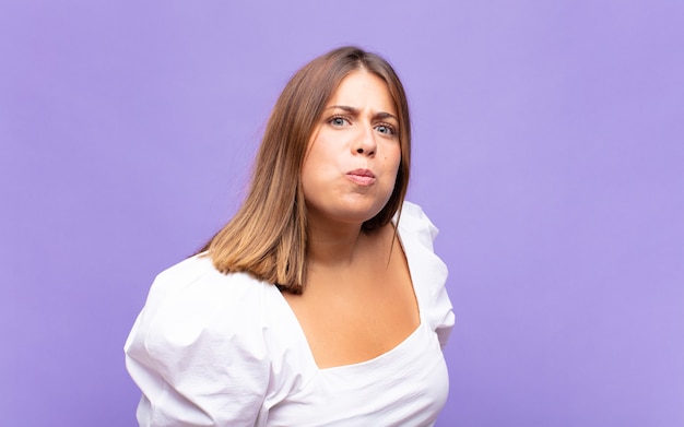 Jovem loira com uma expressão boba, louca e surpresa, bochechas estufadas, sentindo-se recheada, gorda e cheia de comida