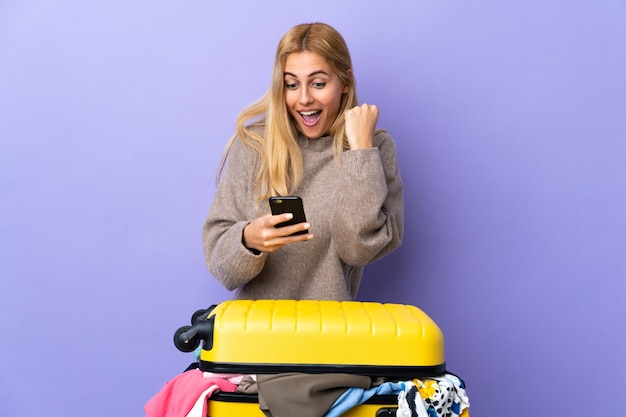 Jovem loira com uma mala cheia de roupas isolada