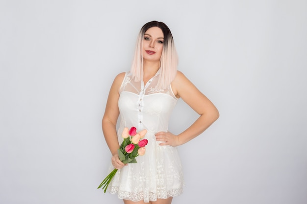 Jovem loira com vestido branco primavera, segurando um buquê de tulipas cor de rosa nas mãos. Conceito de dia das mães. Dia da Mulher. 8 de março